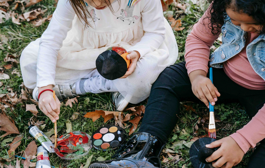 two kids painting pumpkins outside