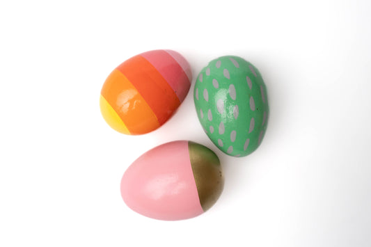Spring wooden eggs: green with lavender spots, pink with gold bottom, and rainbow stripes yellow, red, orange, pink
