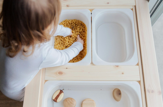 toddler playing with macaroni sensory bin
