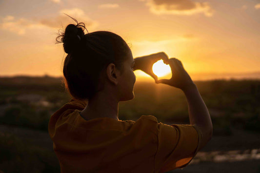 Woman making a heart in the sunset