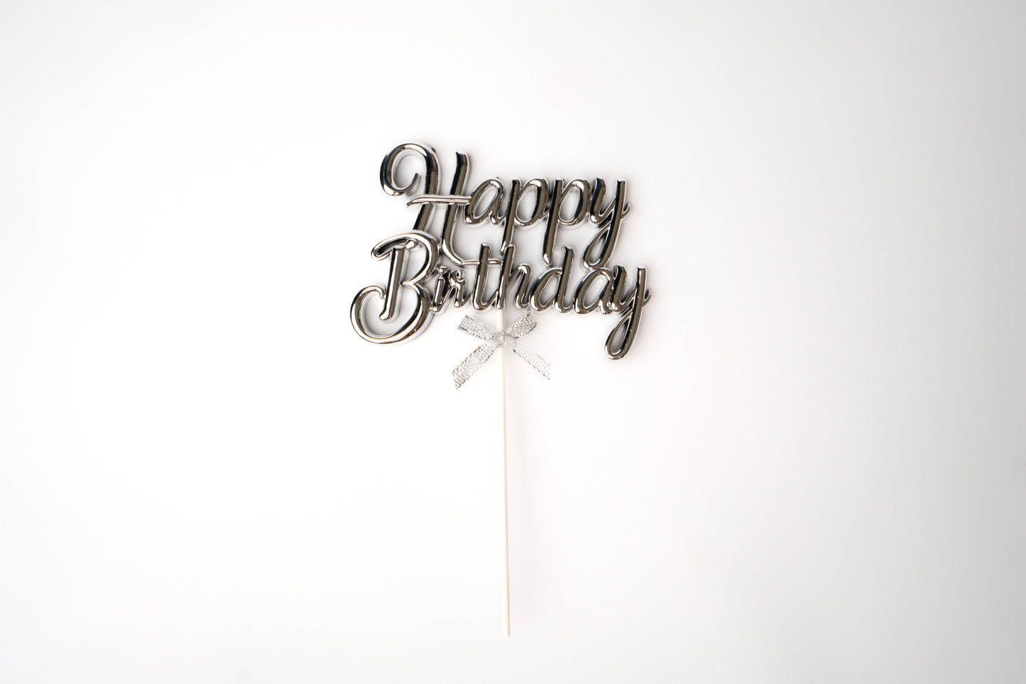 Happy birthday cake topper in silver cursive writing with silver bow